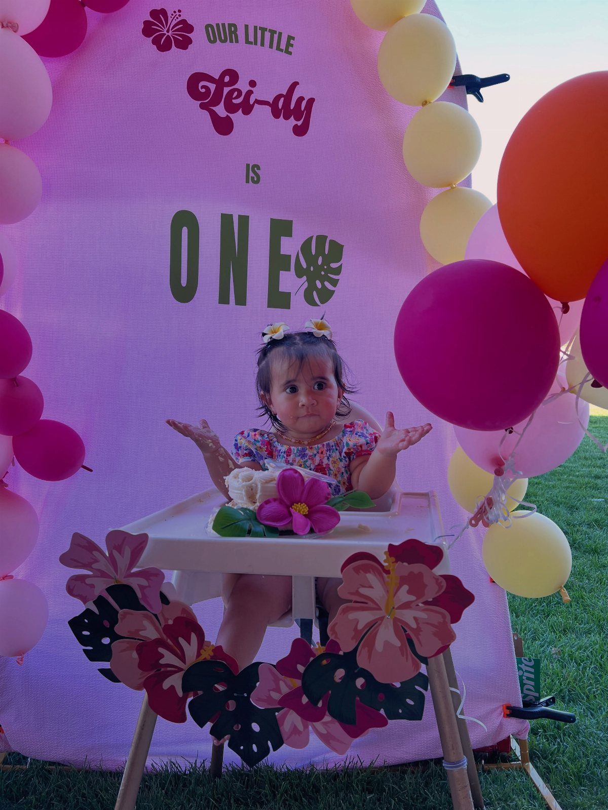 Baby girl at a Hawaiian themed first birthday party with tropical decorations and balloons