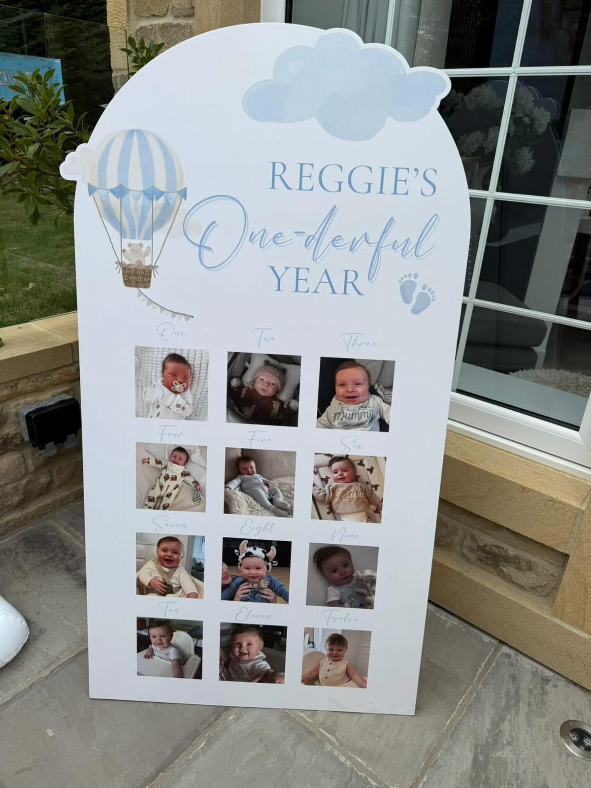 White arched milestone board with monthly baby photos and blue hot air balloon design.