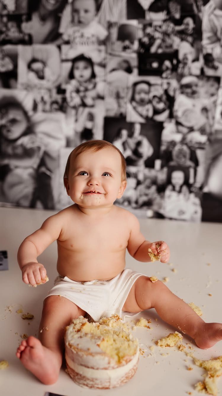 Smiling baby in a diaper sitting with a smashed cake and photo backdrop