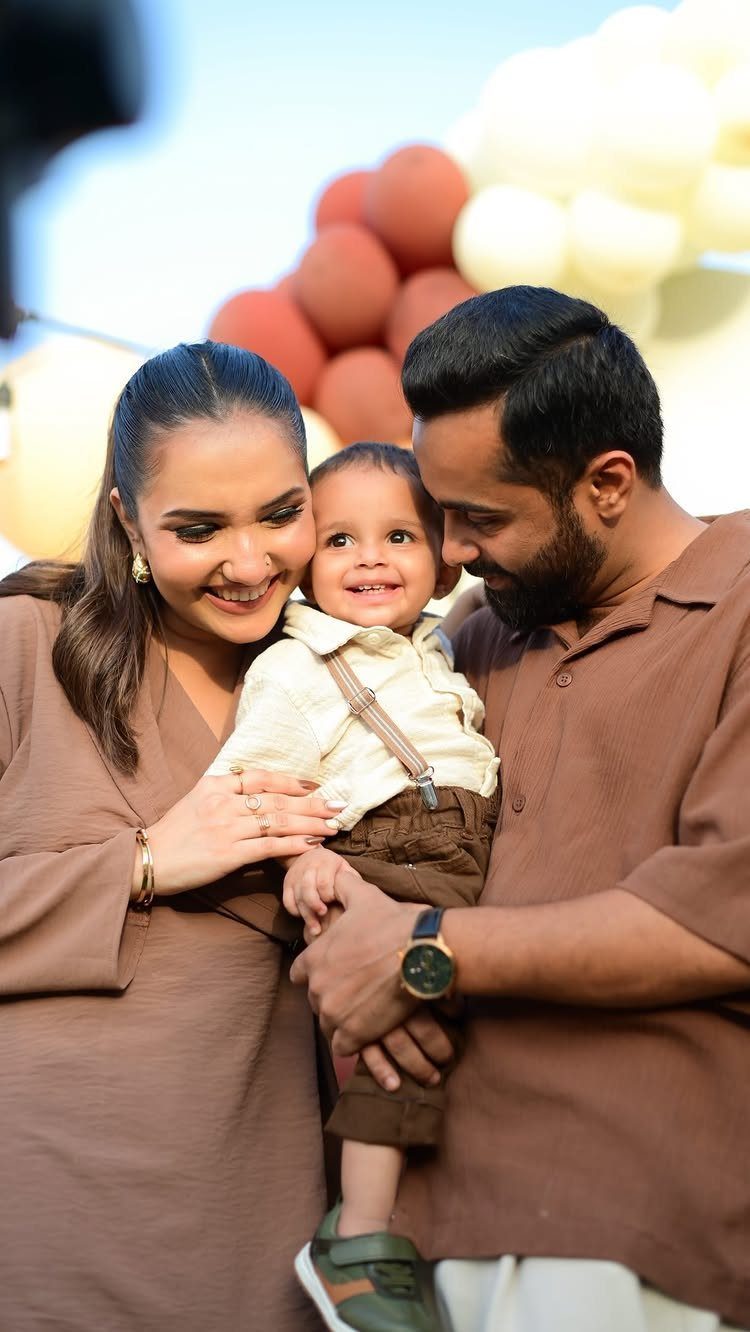 Parents and baby boy posing together in front of white and terracotta balloons.