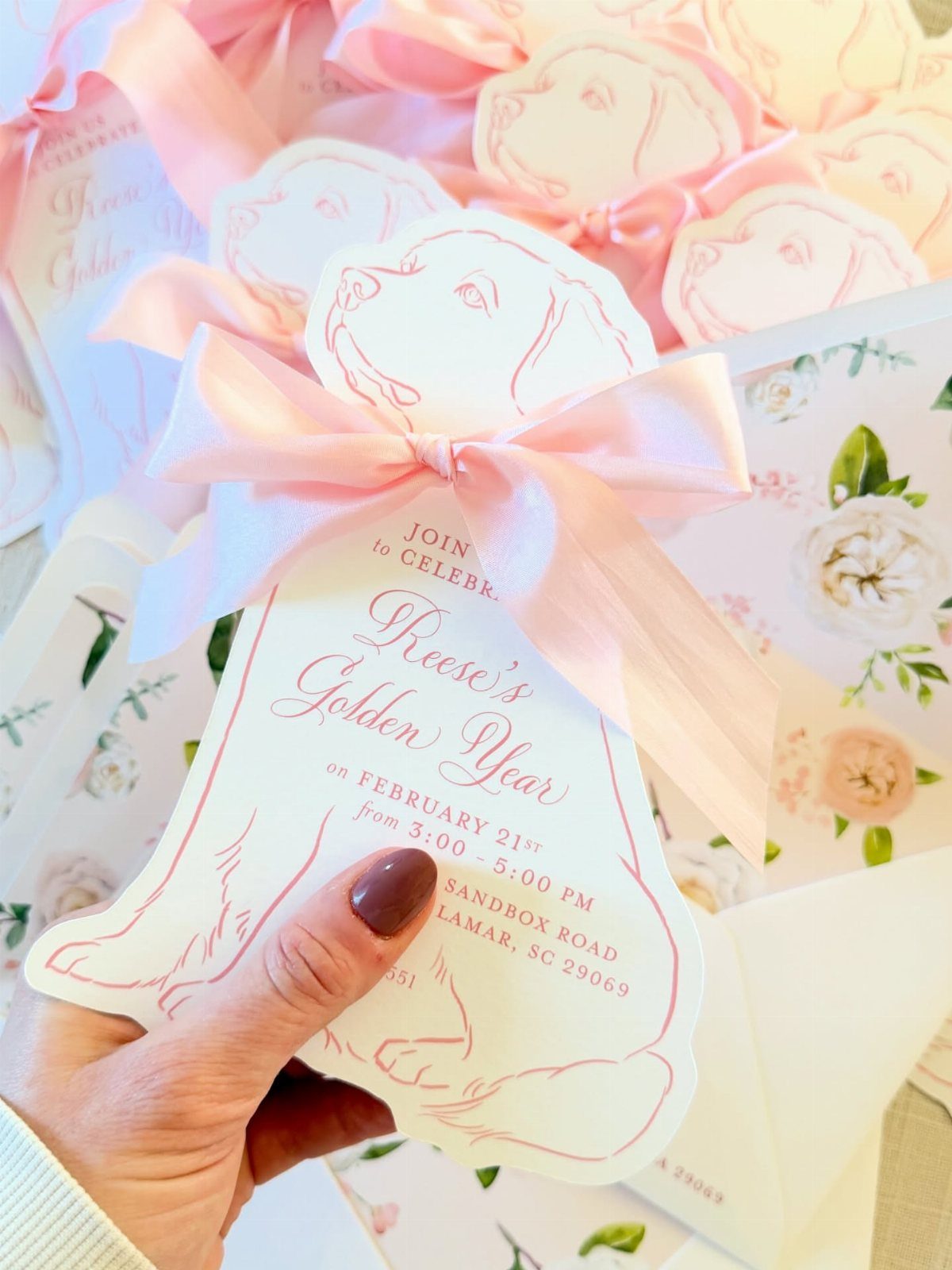 Dog-shaped birthday invitation with a pink bow and floral stationery in background