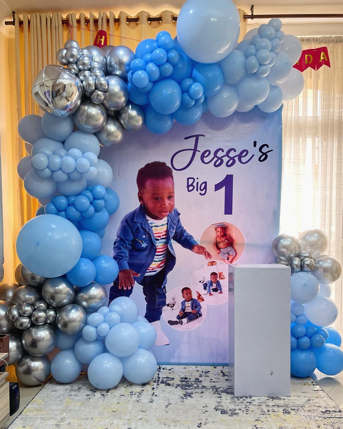 Blue and silver balloon arch surrounding a personalized birthday backdrop for Jesse's first birthday.