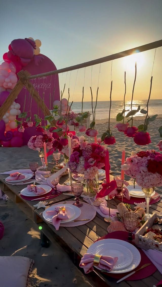 Beach dinner table with pink decorations, flowers, and balloons at sunset