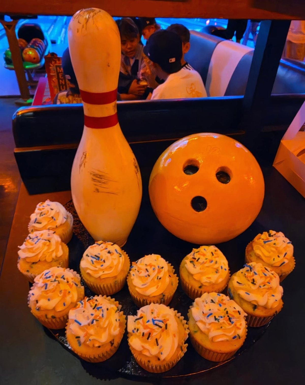 Cupcakes with sprinkles arranged around a bowling pin and ball decoration.
