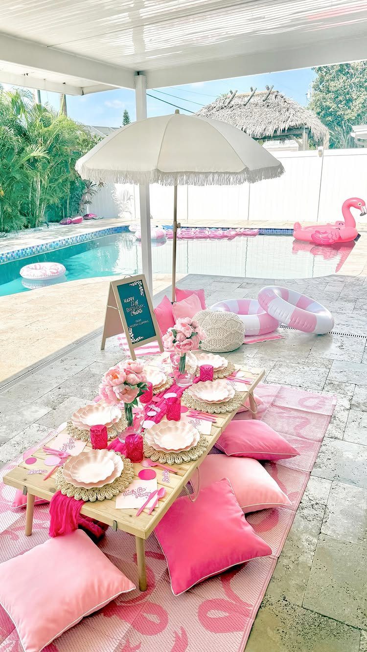 Pink themed party table setup next to a swimming pool with flamingo floats.