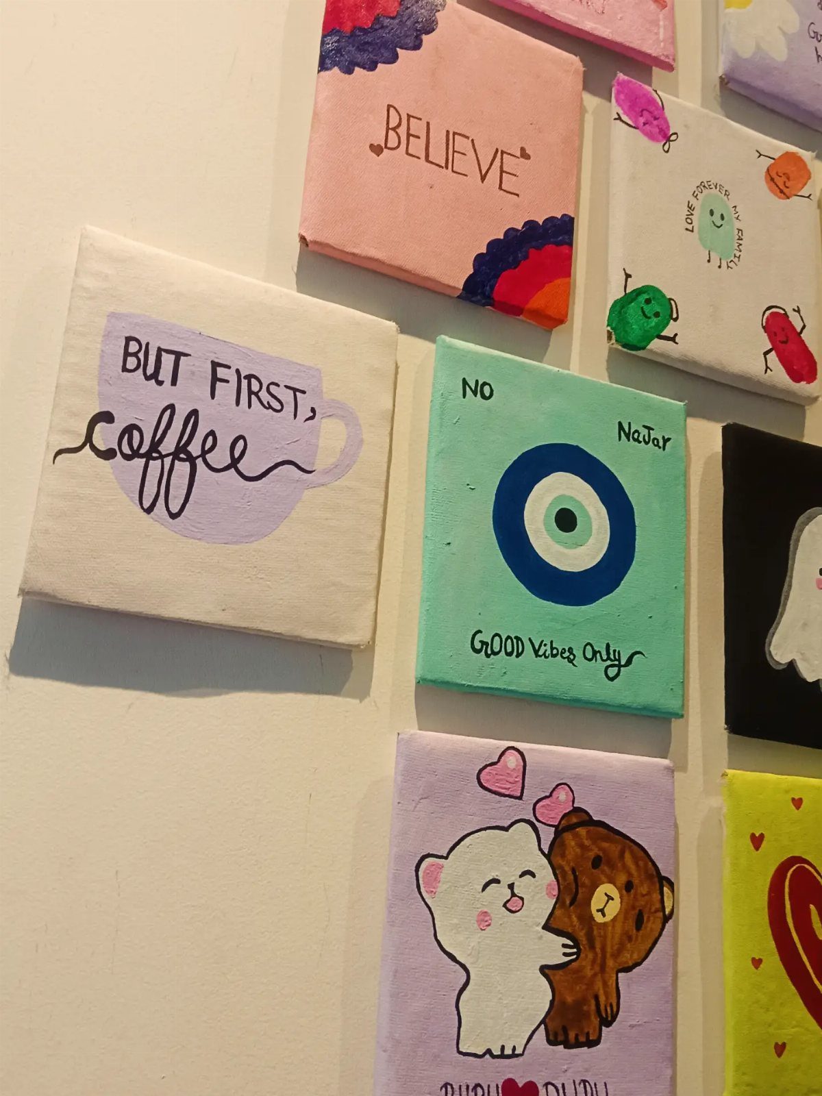 Small painted canvases with colorful art and quotes displayed on a white wall.