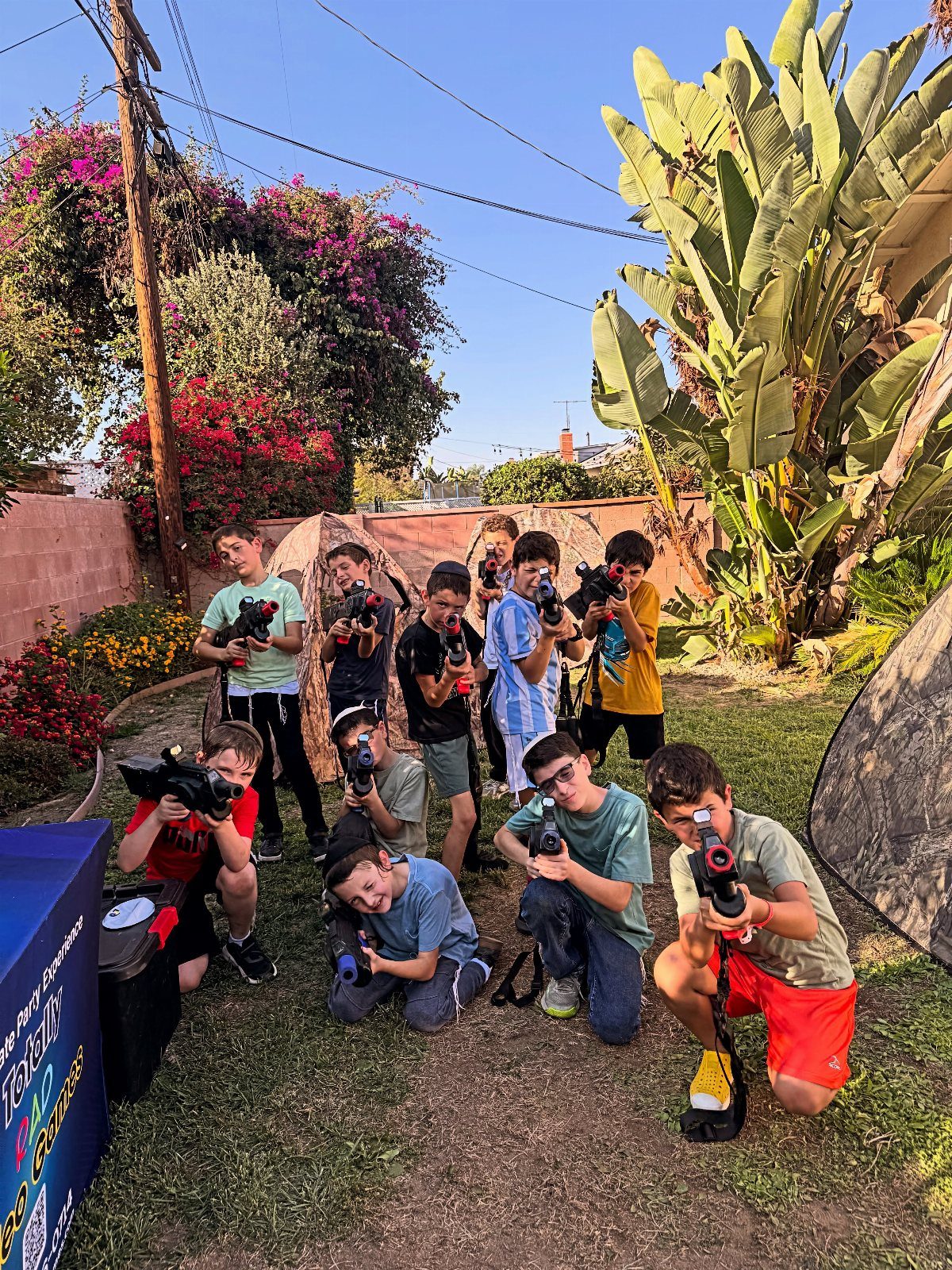 Group of boys holding laser tag guns posing in a sunny backyard garden.