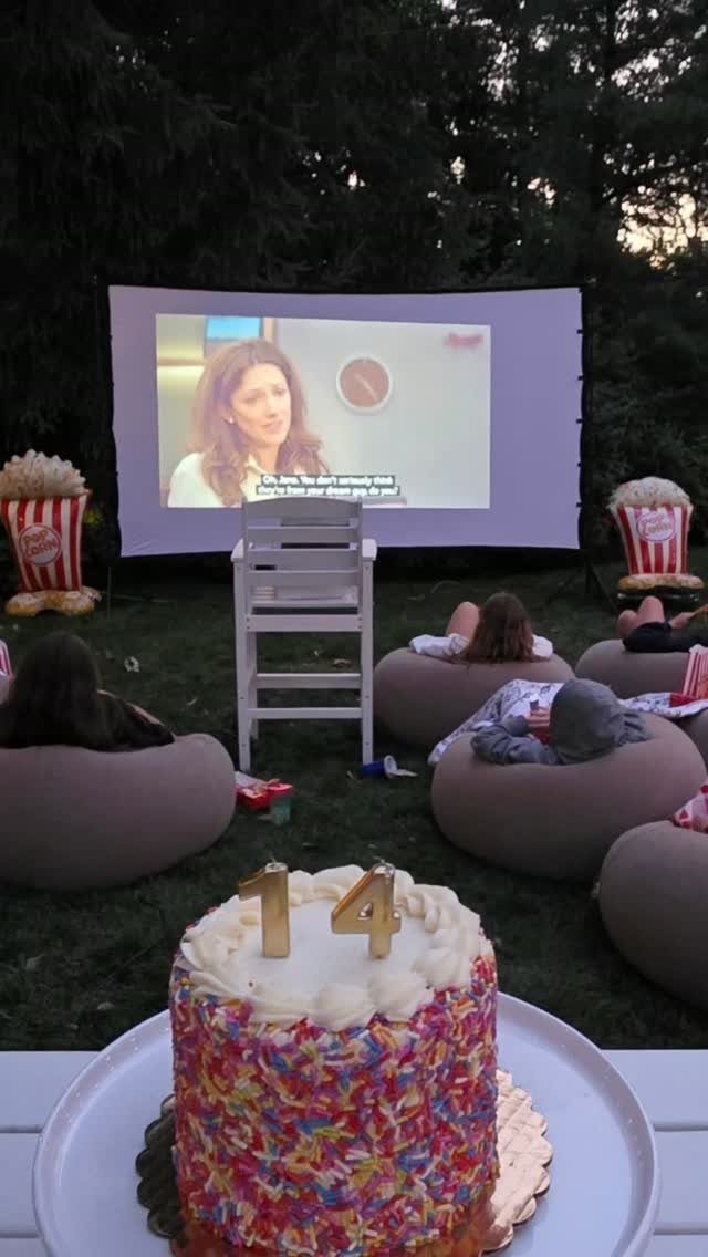 Sprinkle cake with 14 topper in front of outdoor movie screen and beanbags