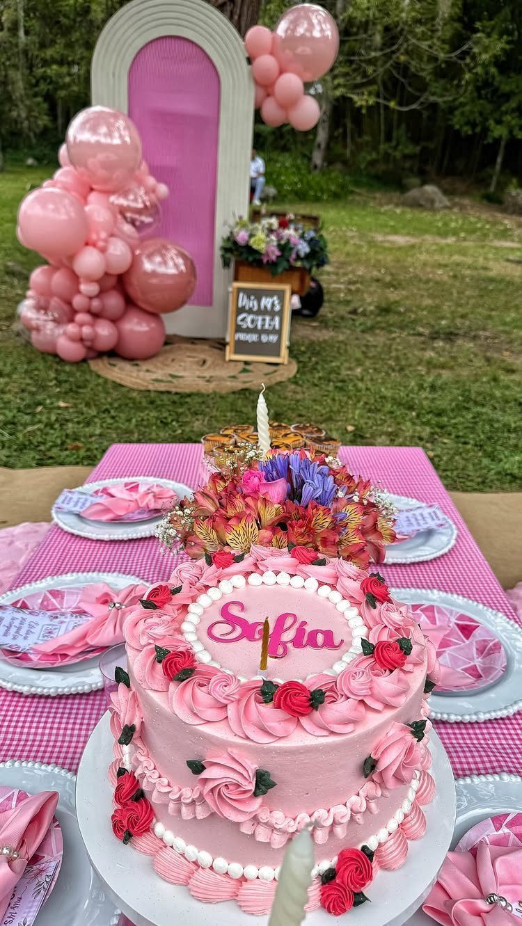 Pink frosted birthday cake with roses on a decorated outdoor party table.