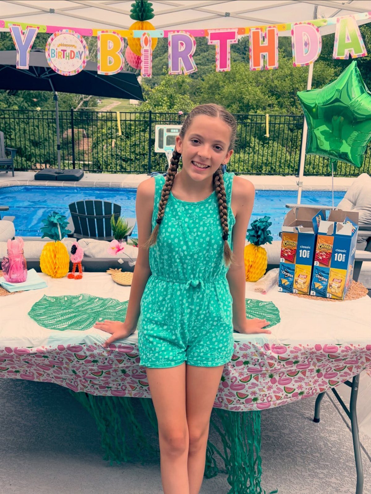 Girl in teal romper standing by a party table next to a swimming pool