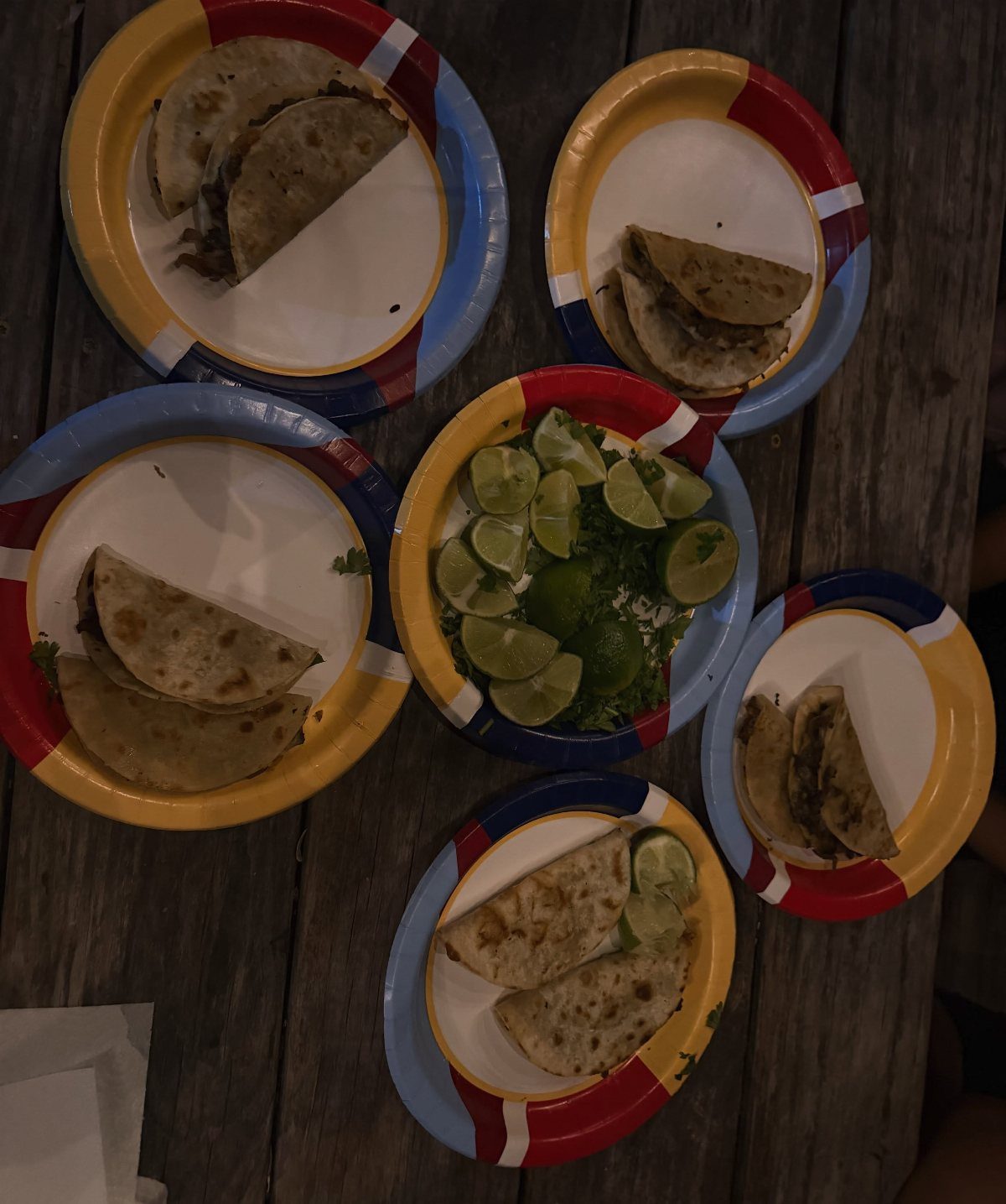 Tacos on colorful paper plates with a center bowl of lime wedges.