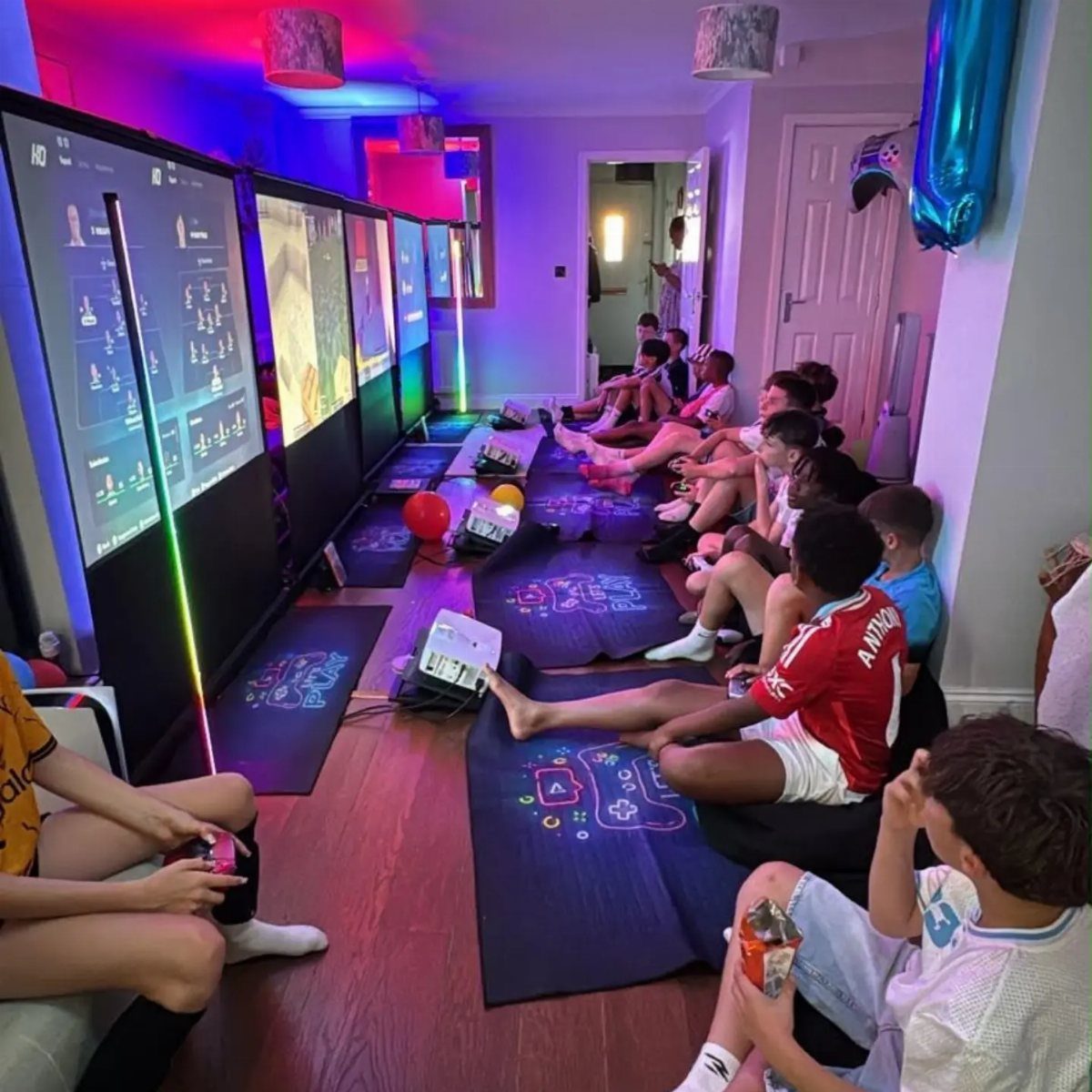 Teenagers playing video games on large vertical screens during a gaming party.