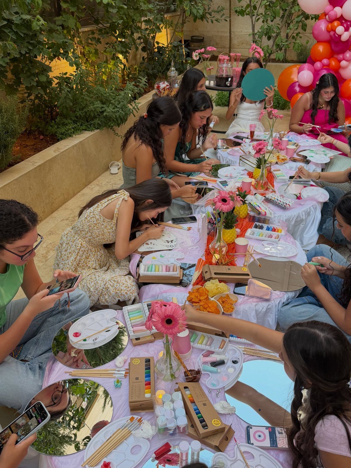 Teenage girls painting on small canvases at a decorated outdoor party table.