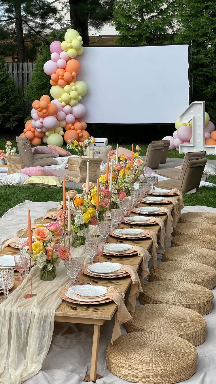Low wooden dining table with floral centerpieces and woven cushions before a projector screen
