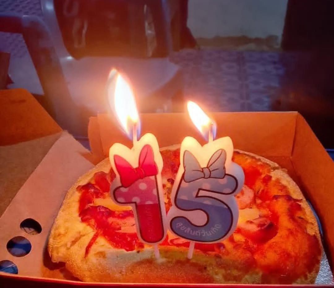 Pizza in a box with lit number 15 birthday candles with bows.
