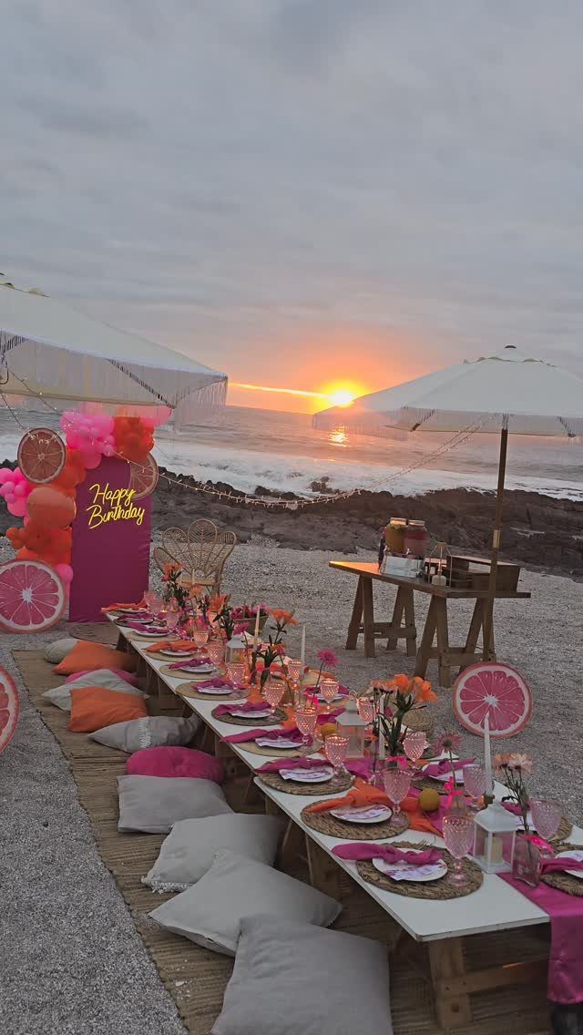 Low wooden beach table with pink decorations and floor cushions at sunset