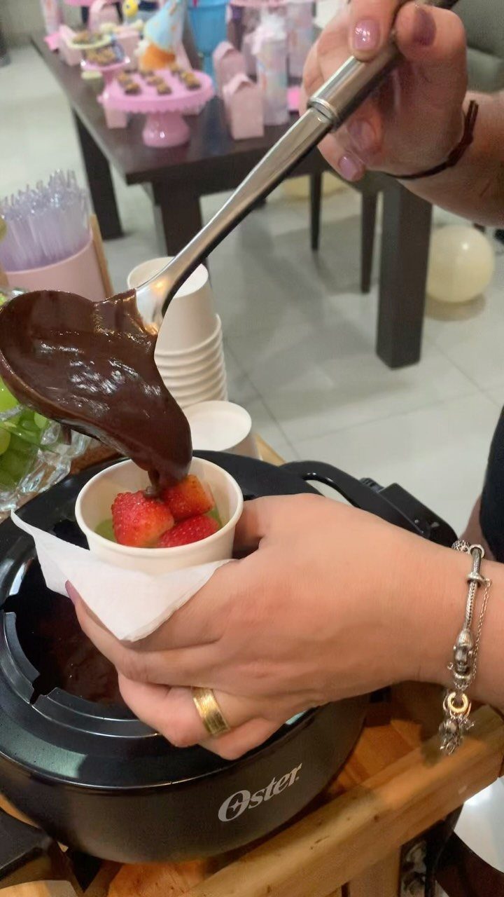 Melted chocolate being poured over strawberries at a decorated birthday party table