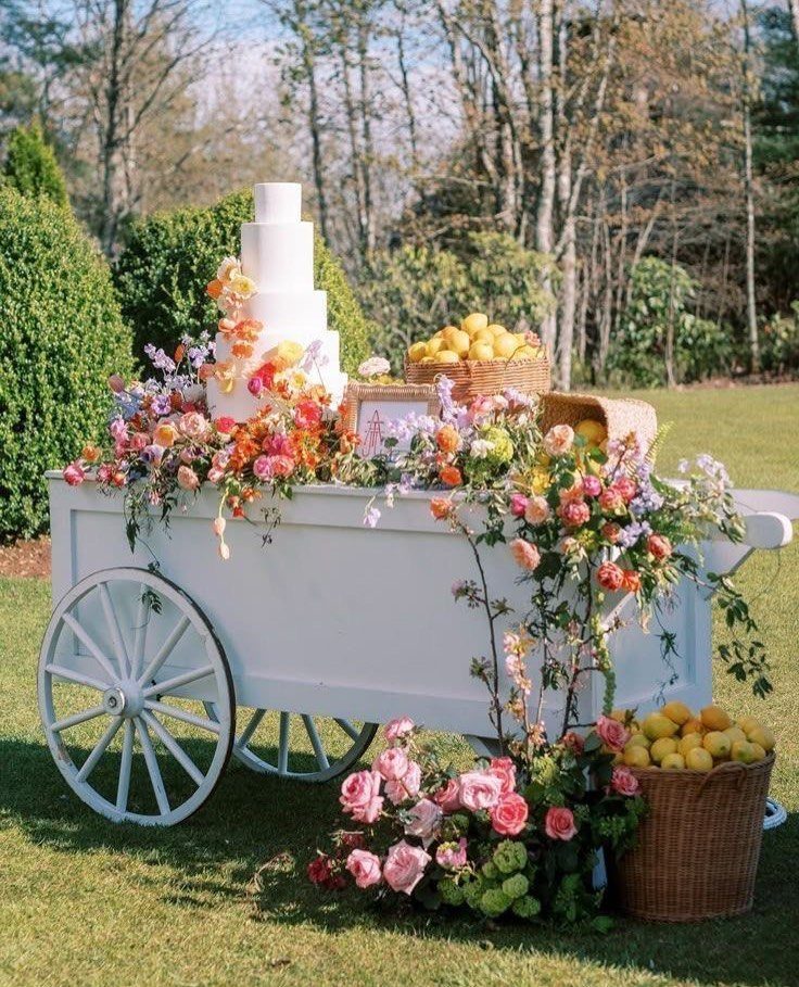 White wooden cart decorated with colorful flowers, lemons, and a tiered white cake.