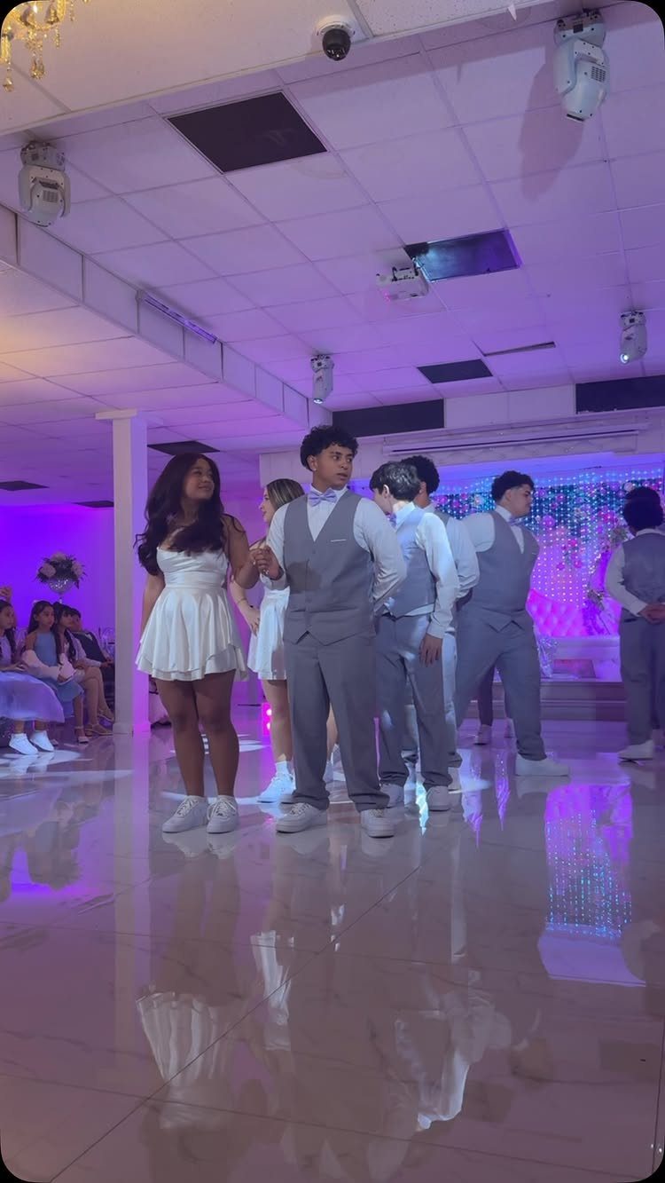 Teenagers in formal wear dancing on a reflective floor with purple ambient lighting.
