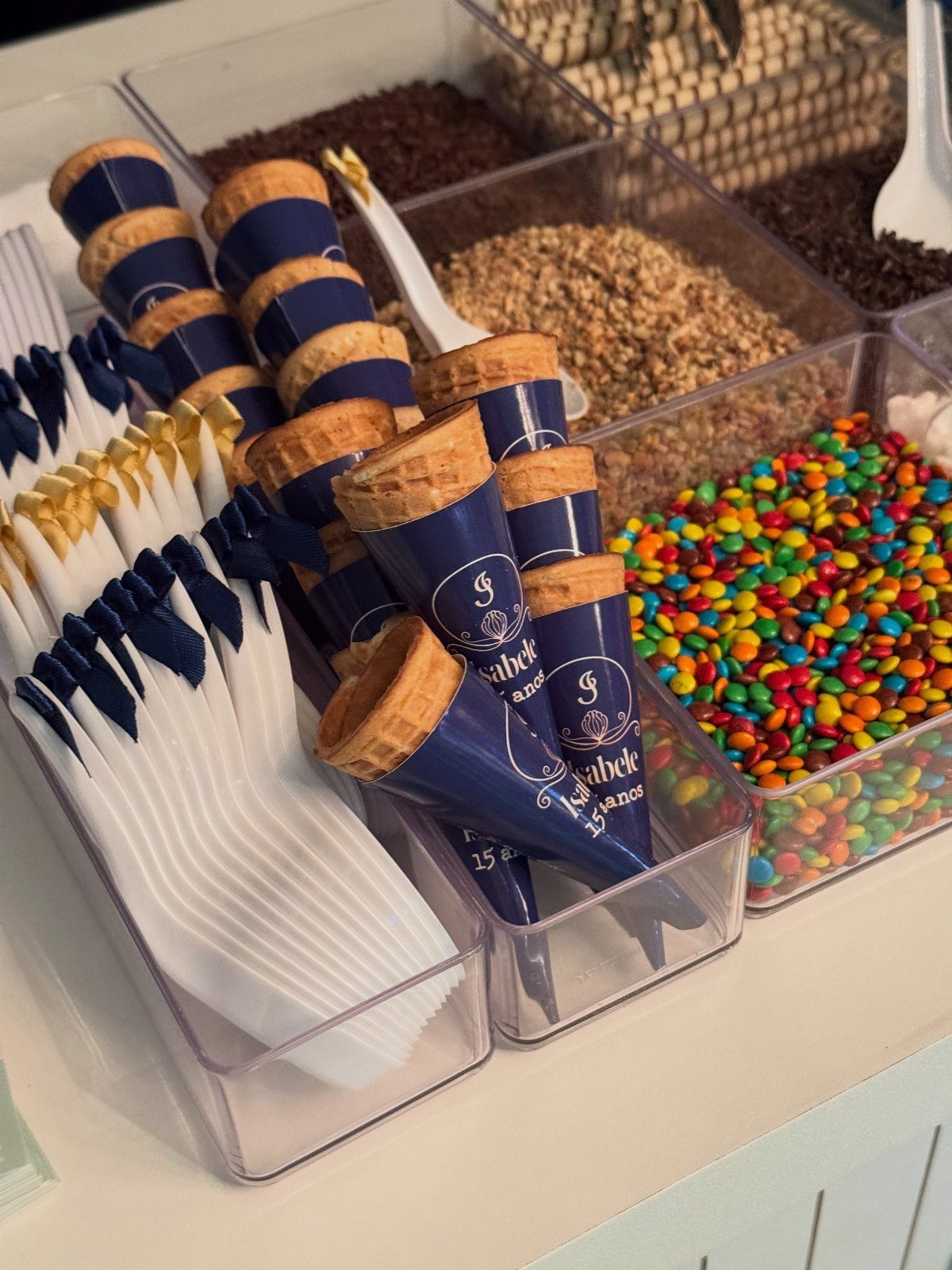Dessert station with blue wrapped waffle cones and bins of colorful candy toppings.