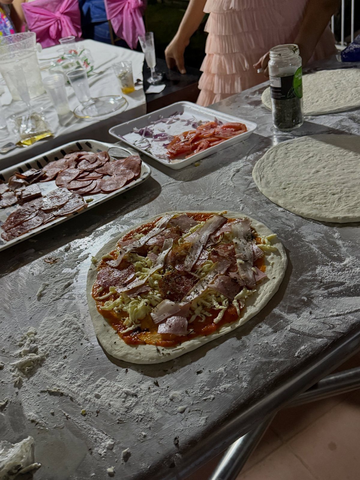 Raw pizza with toppings on a floured metal table during a party setup