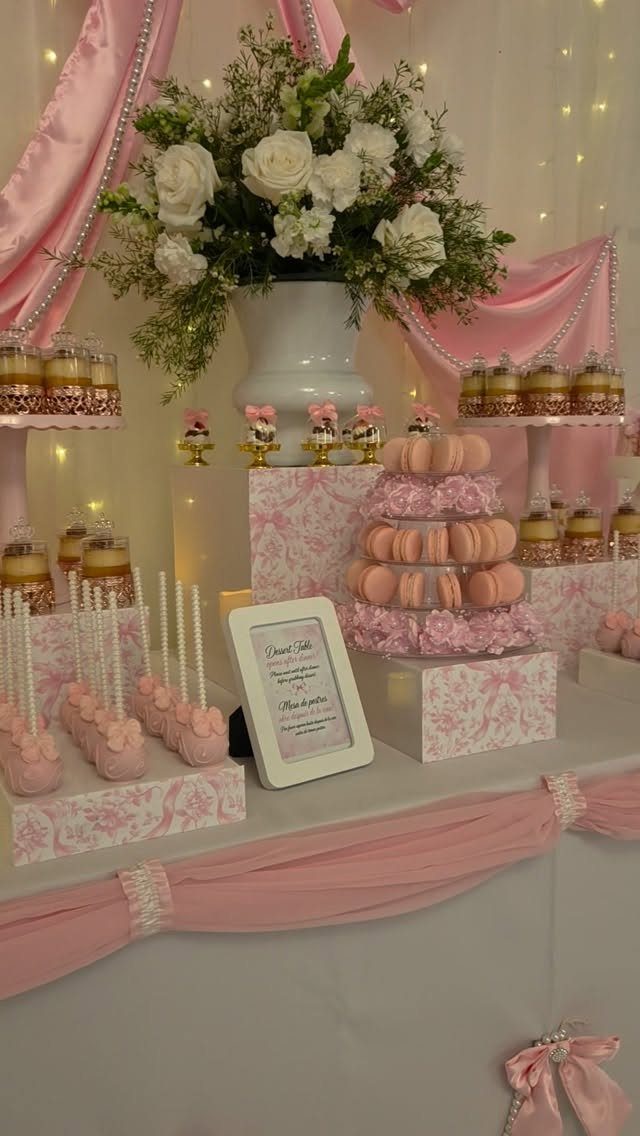 Pink and white dessert table with macarons, cake pops, and white floral arrangement.