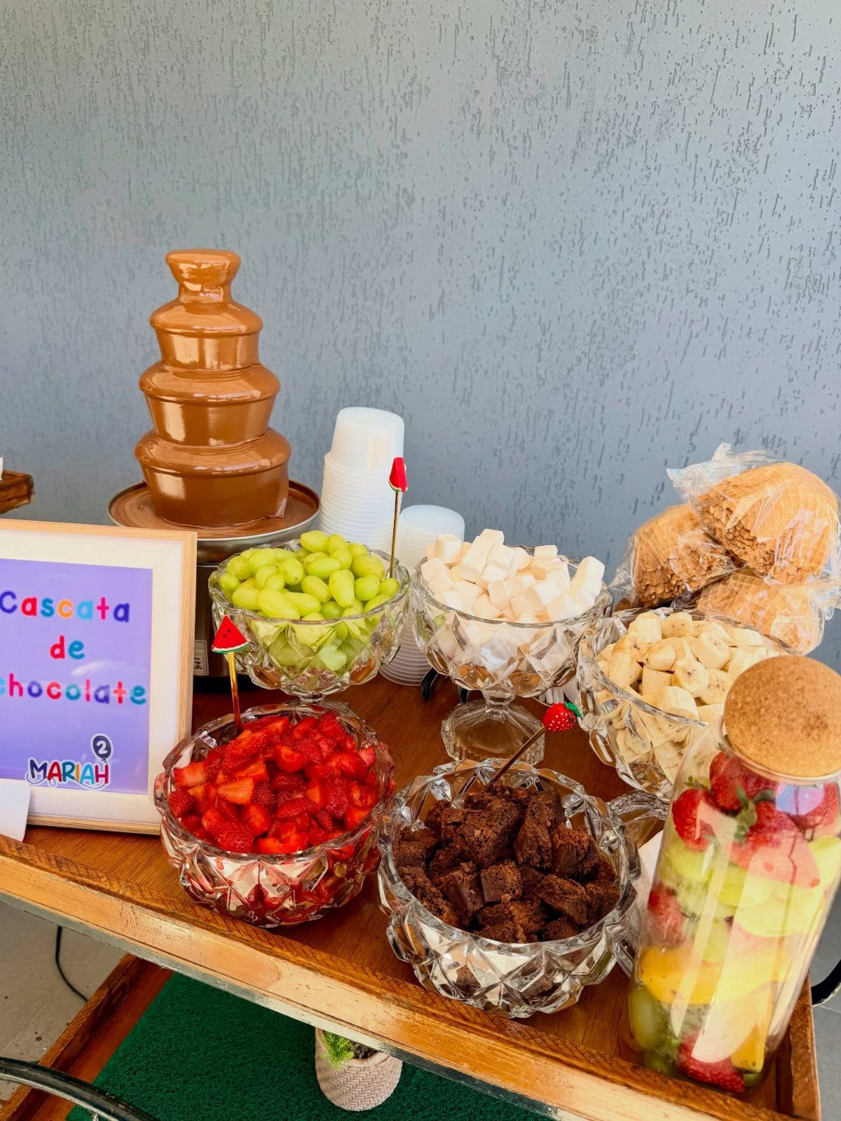 Chocolate fountain with bowls of fresh fruit and brownies on a wooden table