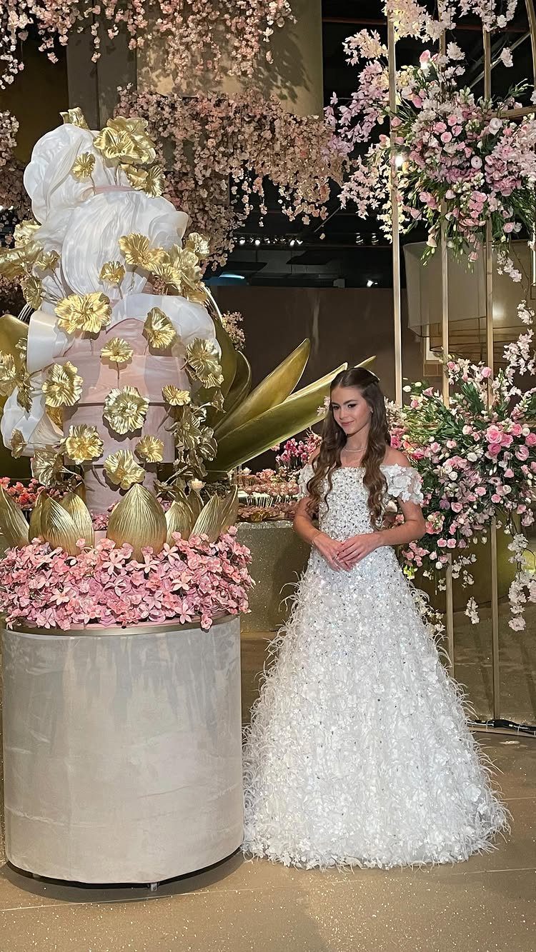 Teenage girl in white ballgown standing beside a large gold and white cake.