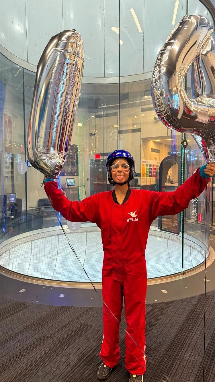 Person in red flight suit and helmet holding silver balloons by wind tunnel