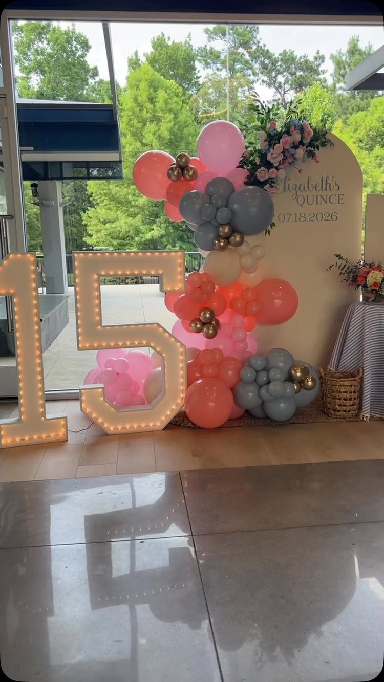 Large light-up number 15 next to a pink and grey balloon arch backdrop.