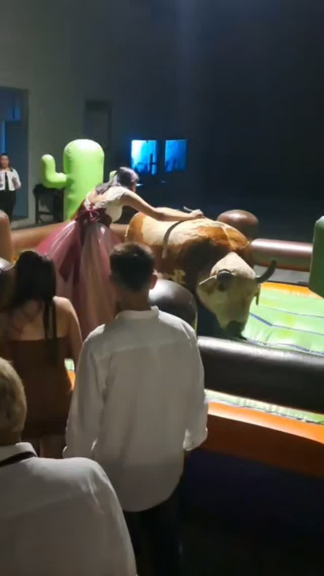 Woman in a pink dress riding a mechanical bull at an indoor party