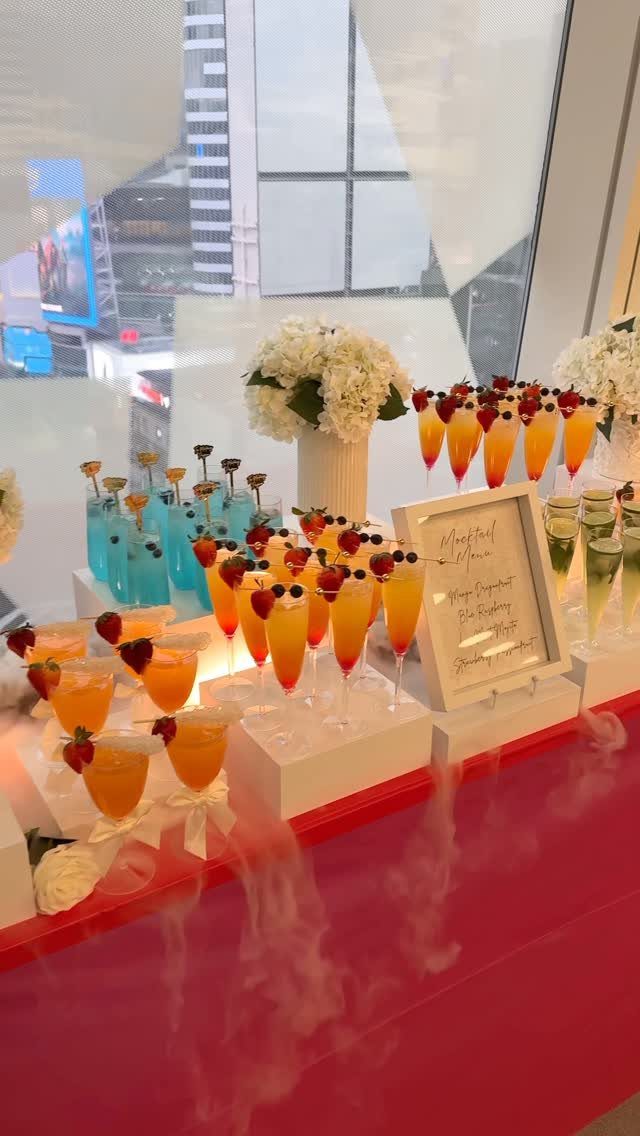 Colorful mocktails with berry garnishes arranged on white platforms with white flowers.
