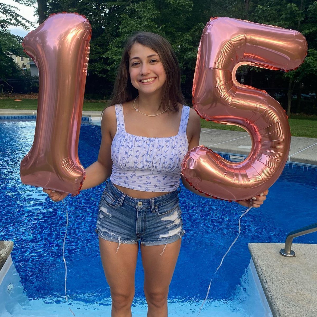 Teenage girl holding rose-gold 15 balloons while standing in a swimming pool