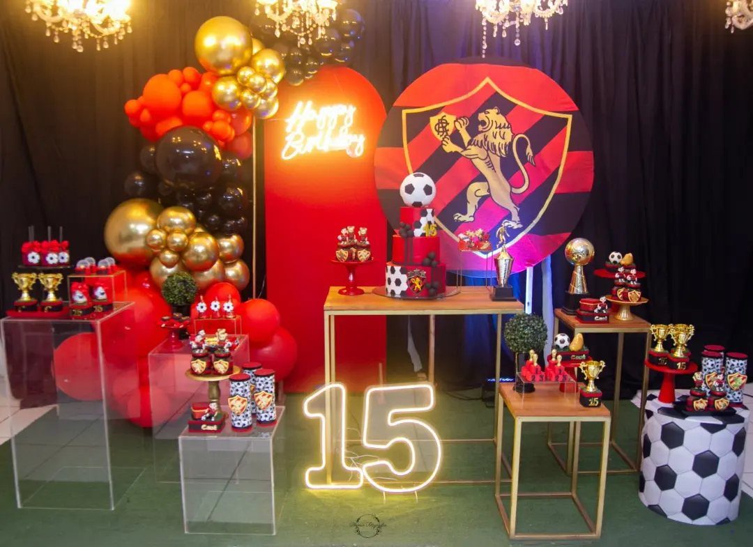 Soccer themed 15th birthday party decoration with red balloons, trophies, and glowing number 15