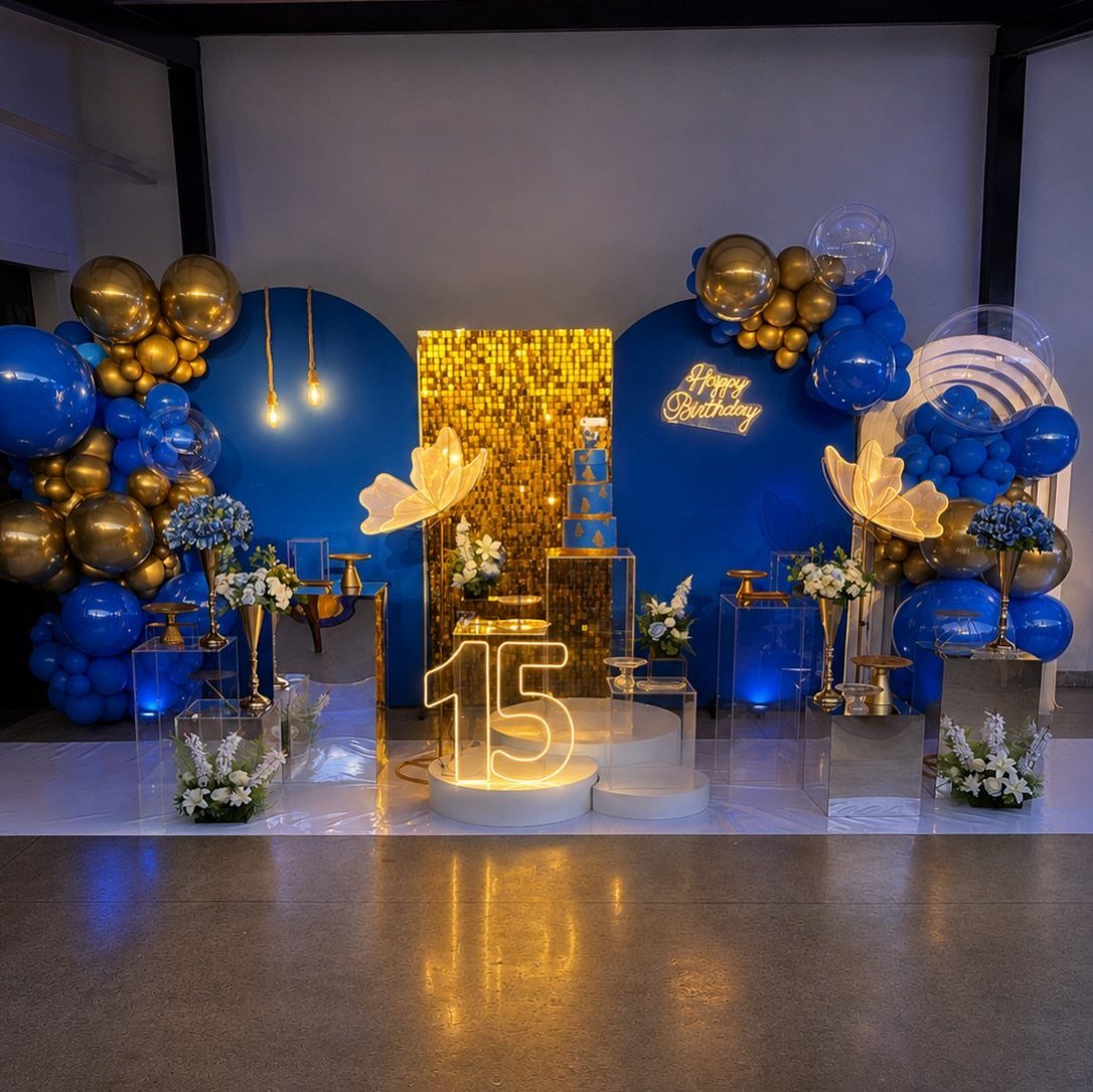 Blue and gold birthday party decoration with balloons and a glowing number 15.