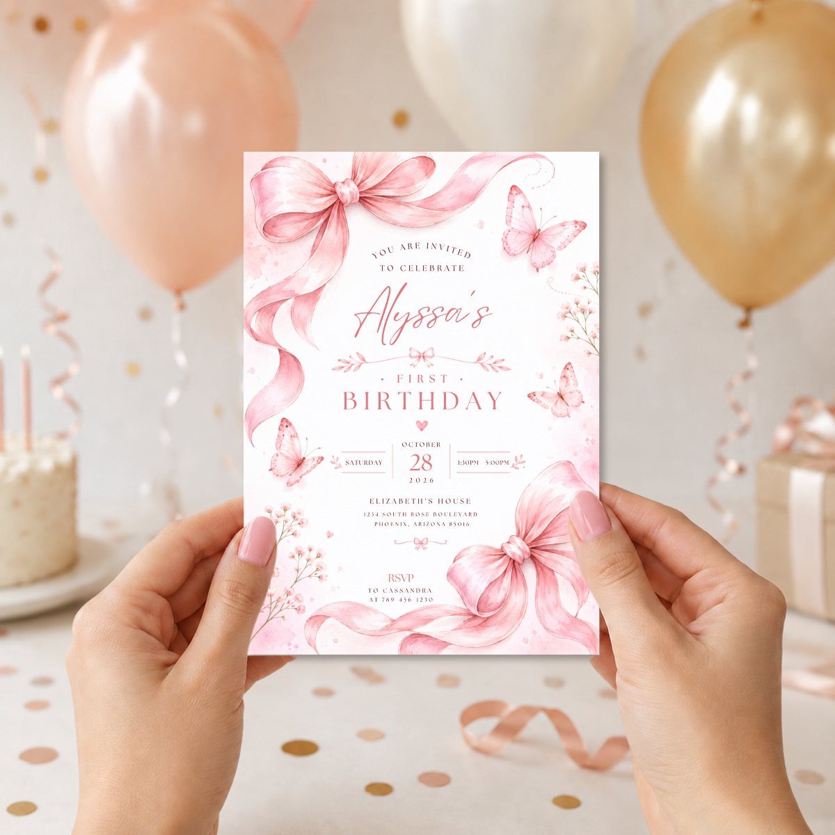First birthday invitation card with pink bows and butterflies held by two hands.