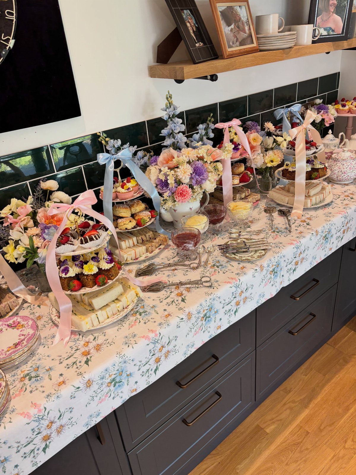 Floral tea party spread with tiered cakes, sandwiches, and colorful flower bouquets.