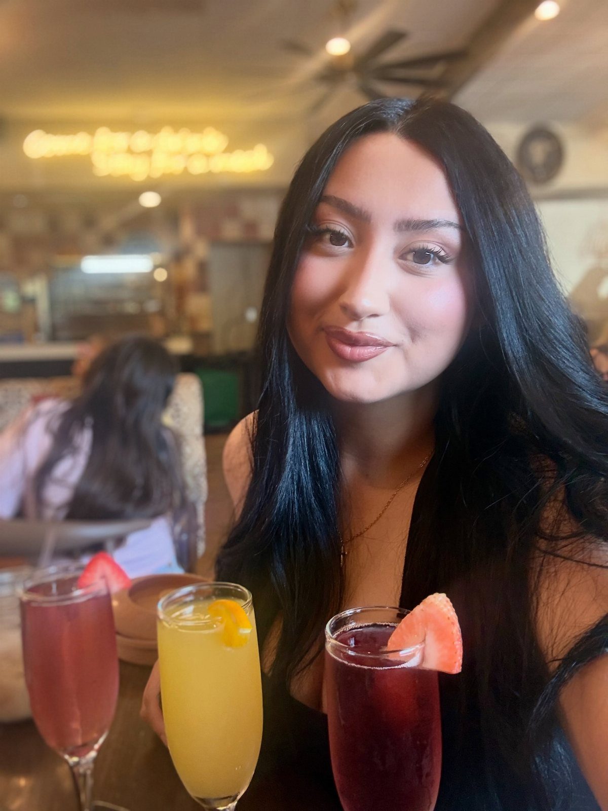 Young woman posing with three colorful cocktails in a restaurant setting.