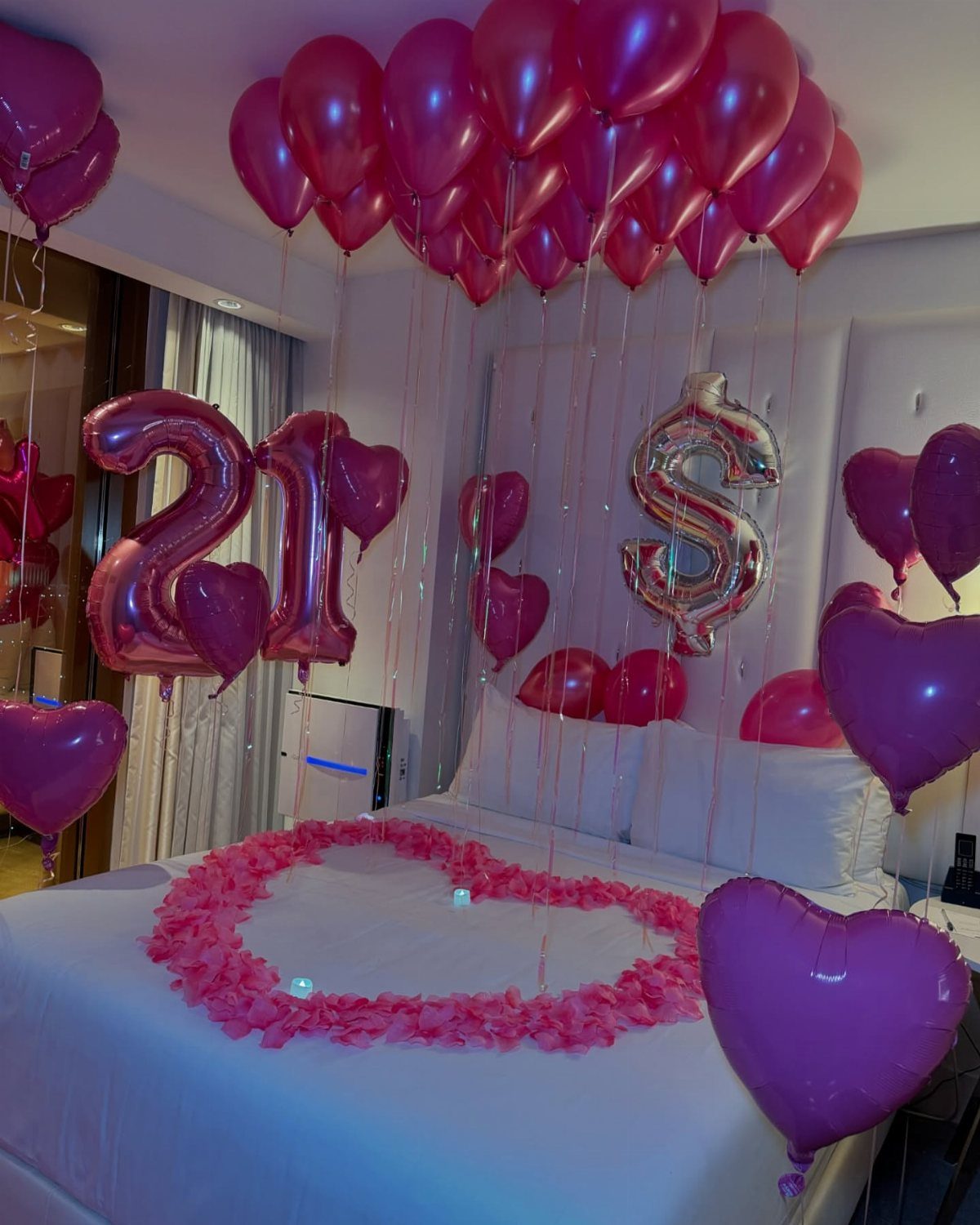 Hotel bed decorated with pink rose petals and balloons for a 21st birthday.