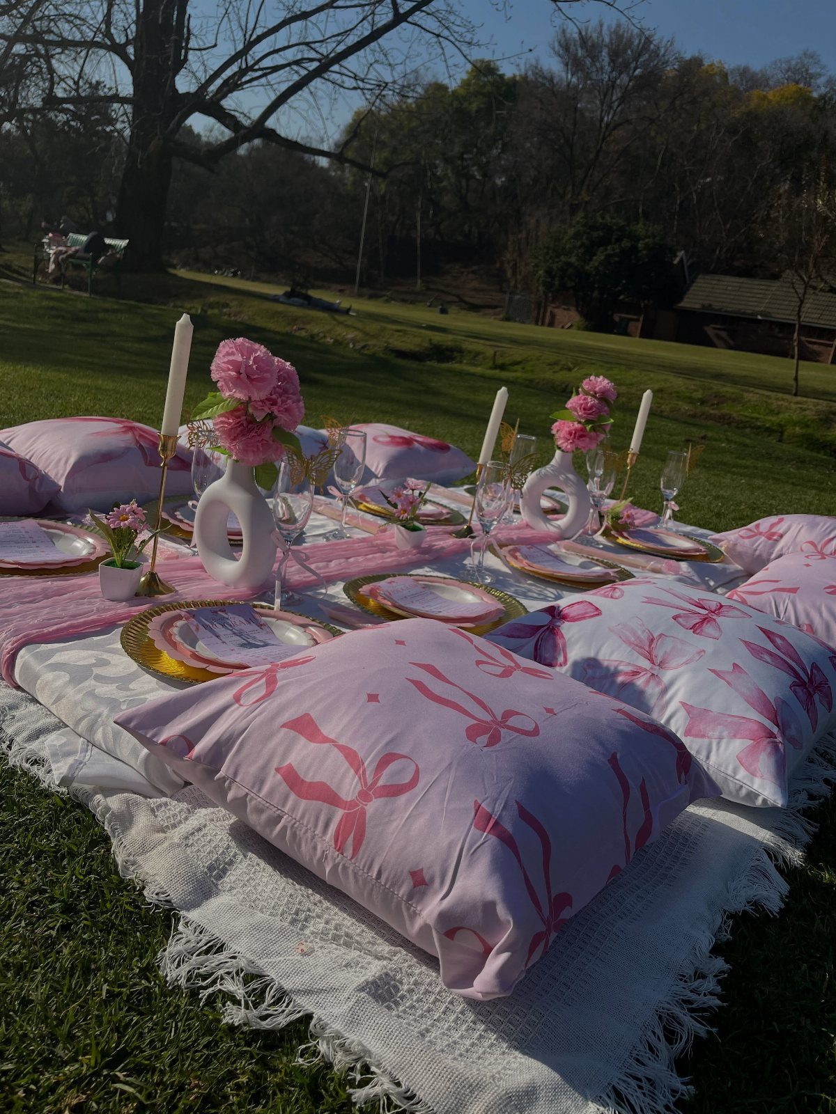 Low picnic table with pink decorations, gold plates, and pillows on a lawn