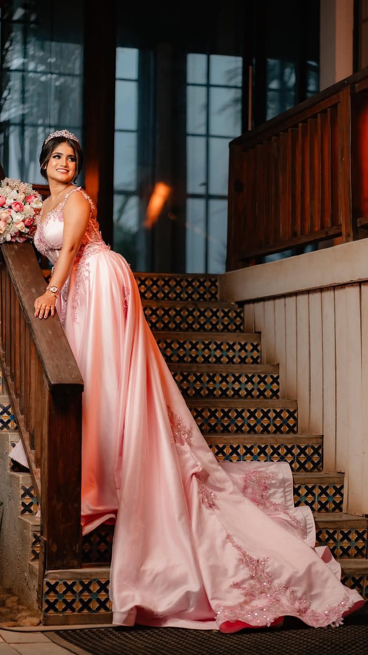 Woman in a pink satin gown and tiara posing on a patterned staircase.