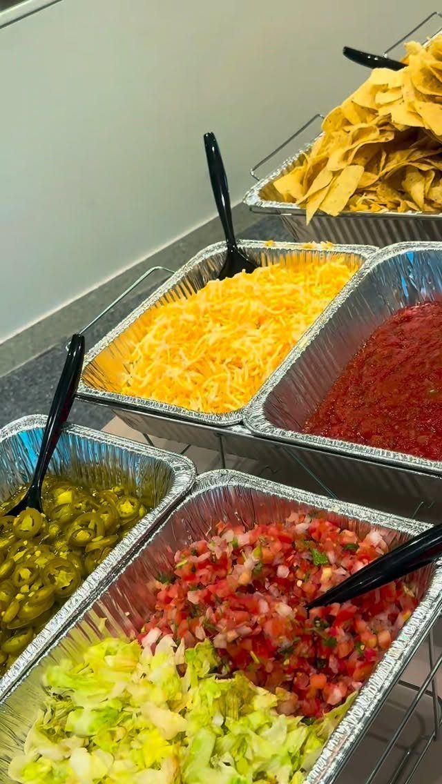 Taco bar setup with trays of lettuce, salsa, cheese, jalapeños, and tortilla chips.