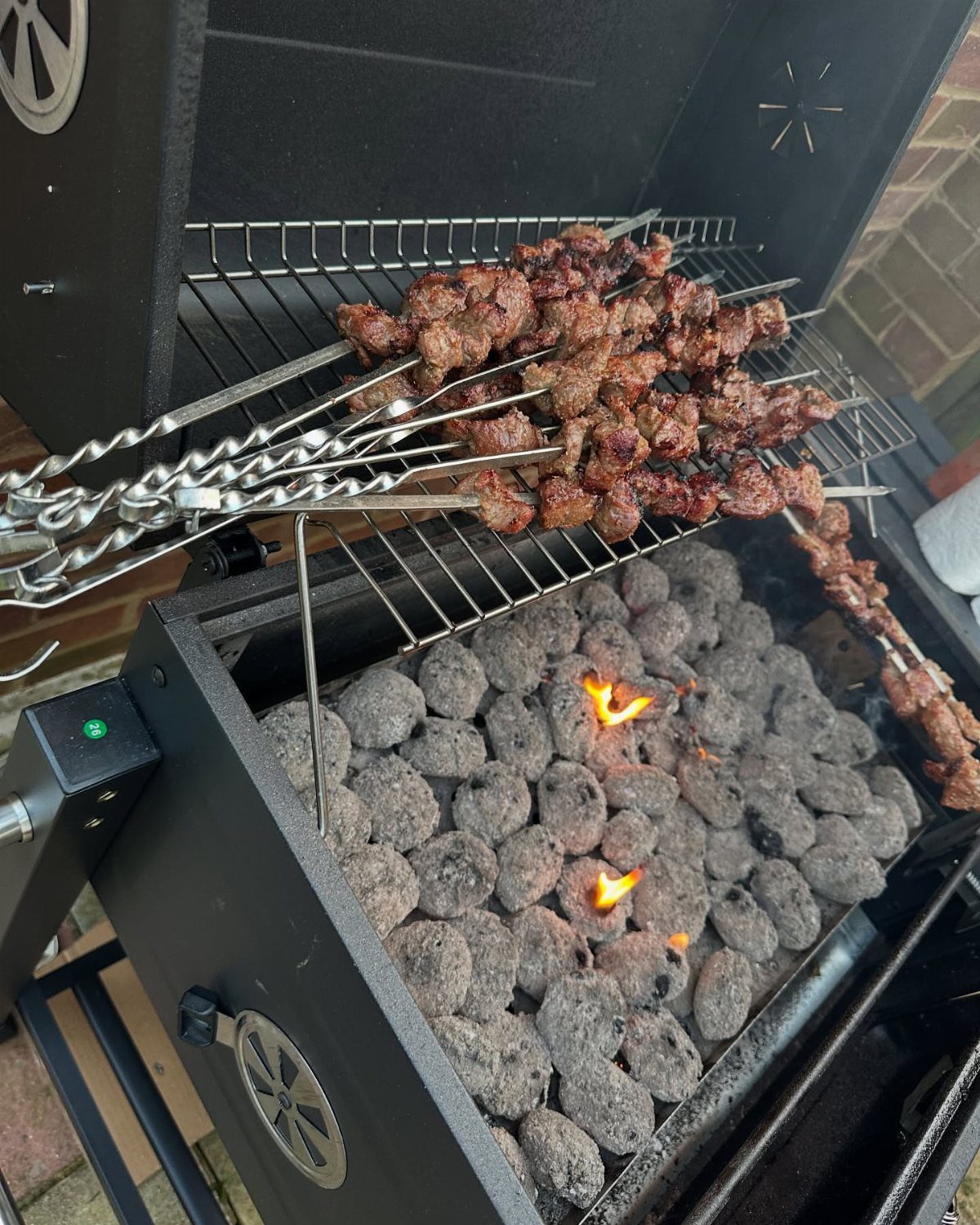 Meat skewers grilling over hot charcoal briquettes in a black outdoor grill