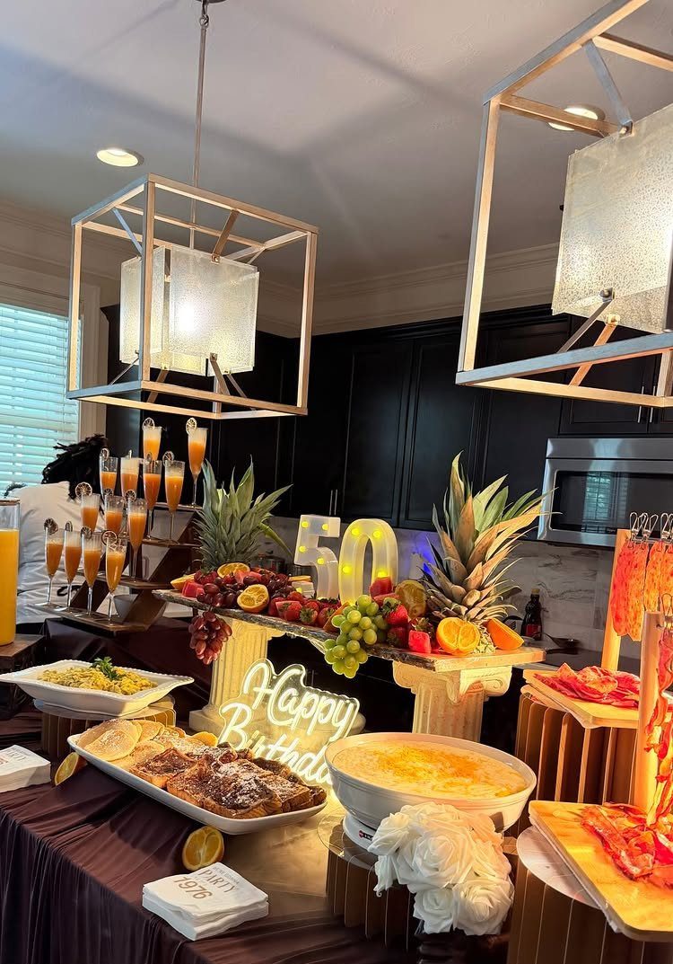 Brunch food spread with mimosas, fruit, and a glowing 50th birthday sign.