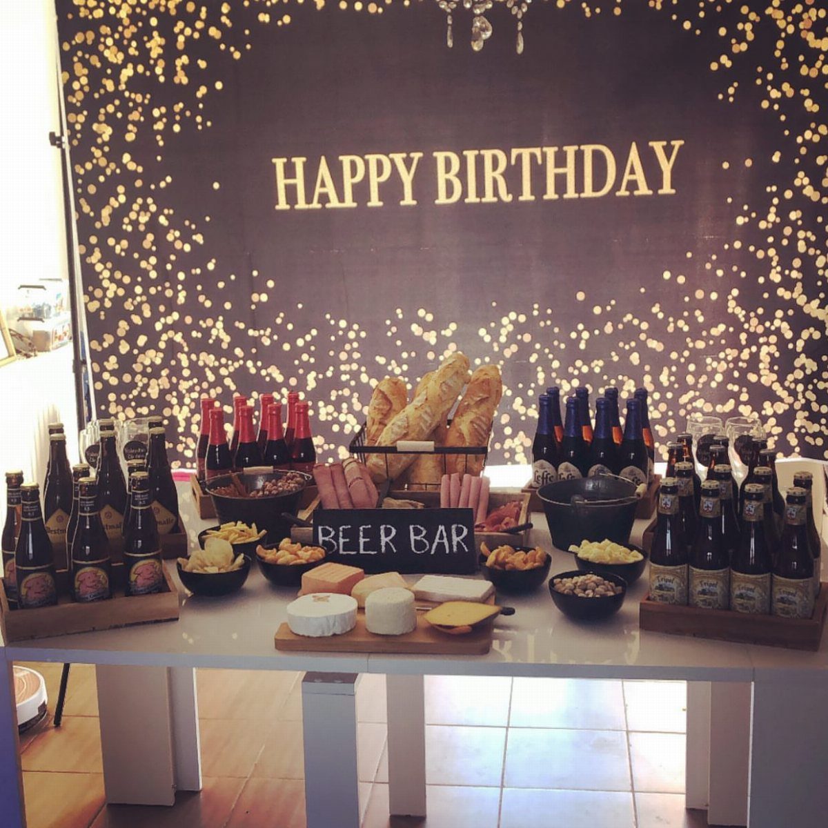 Beer bar setup with bottled beers, snacks, and cheese against a birthday backdrop.