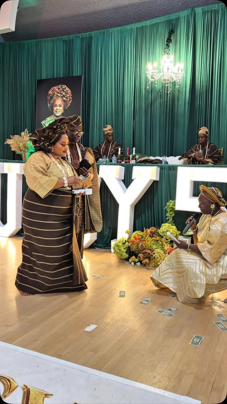 People in traditional West African Kente attire celebrating in a room with green curtains.