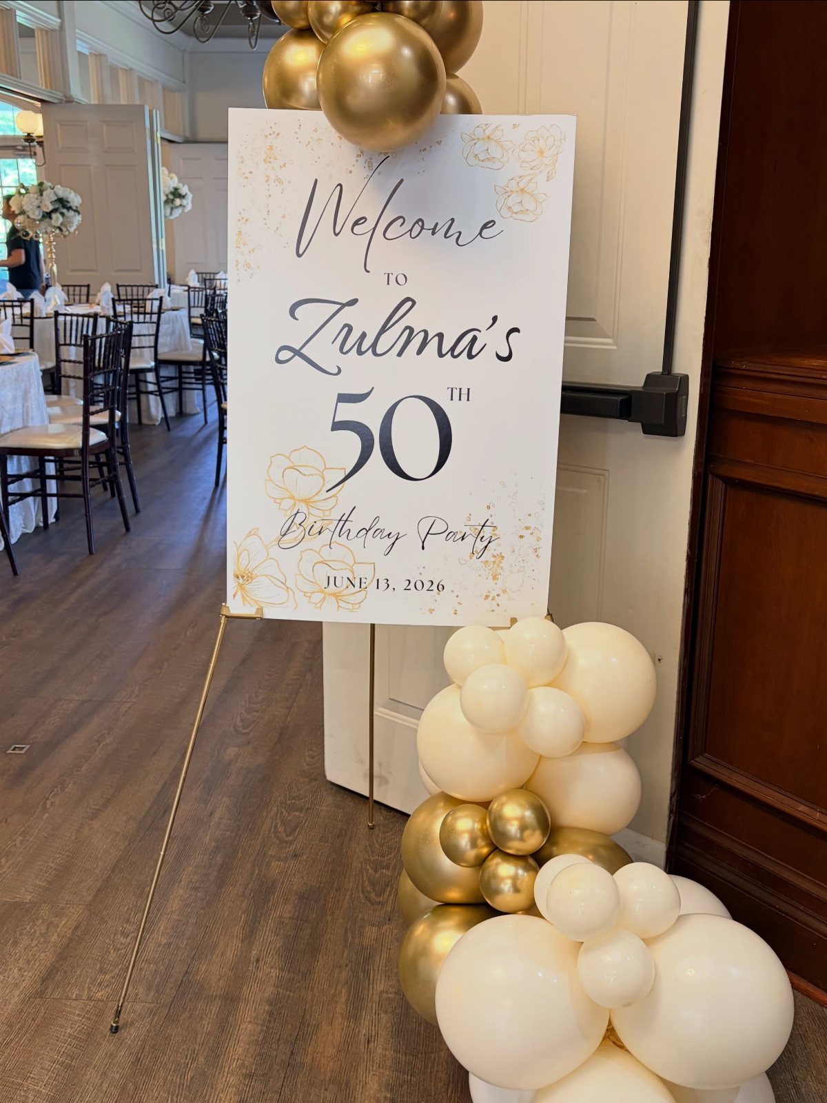 Welcome sign for a 50th birthday party with gold and cream balloons.