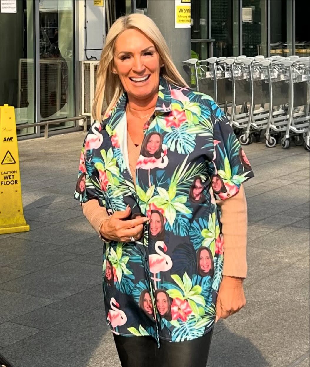 Woman wearing a custom tropical shirt with faces and flamingos standing outdoors.