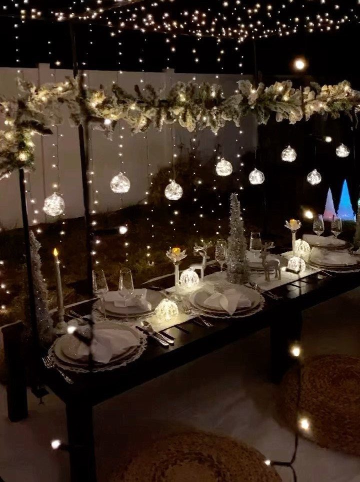 Outdoor dinner table set at night with fairy lights and white tableware.