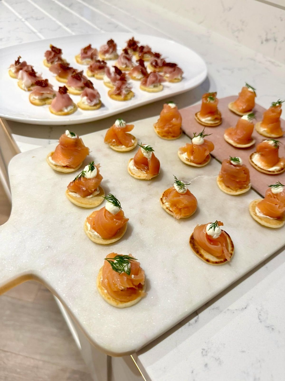 Smoked salmon and prosciutto appetizers arranged on marble platters for a party.